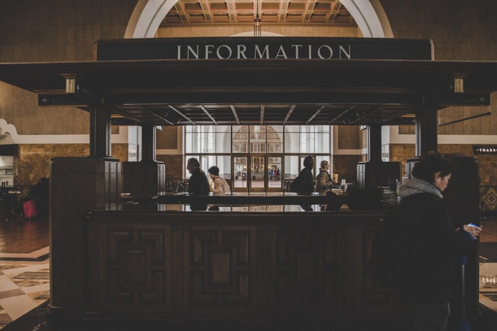 Dunkler Informationsschalter mit Silhouetten von Passanten in großer Halle.
