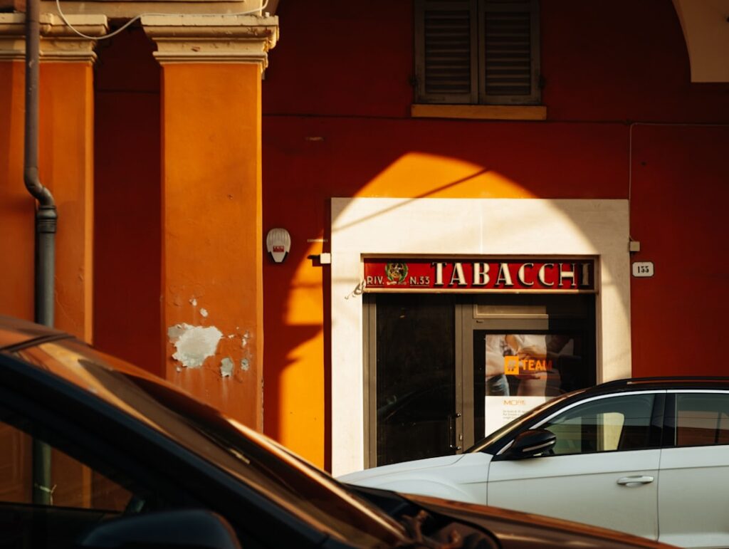 Oranje gevel met 'TABACCHI'-bord en geparkeerde auto's in Modena.