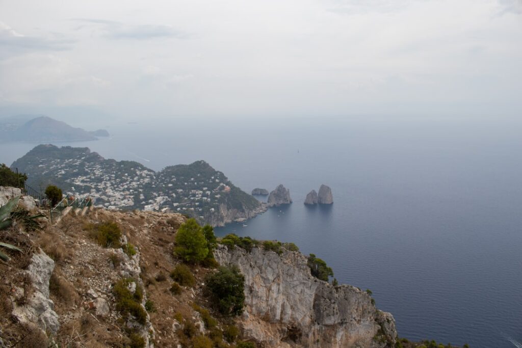 Panoramic Capri coastline from cliffs with Faraglioni sea stacks visible.