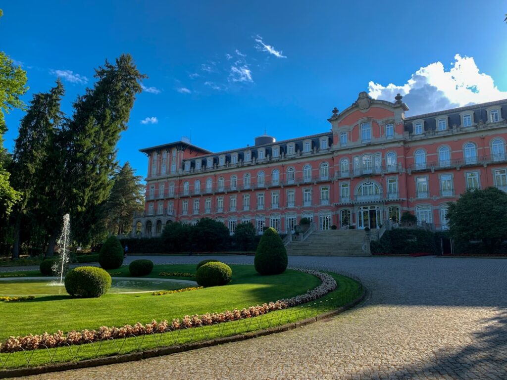 Grand pink neoclassical hotel façade with fountain and manicured lawn.