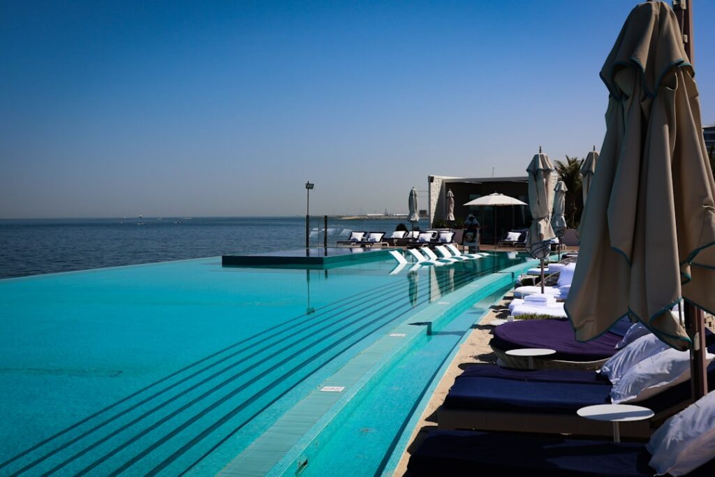 Oceanfront infinity pool with sunbeds and umbrellas beside calm sea.