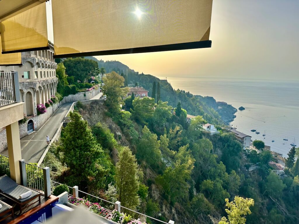 Terrasse d'hôtel ombragée donnant sur la côte boisée de Capri