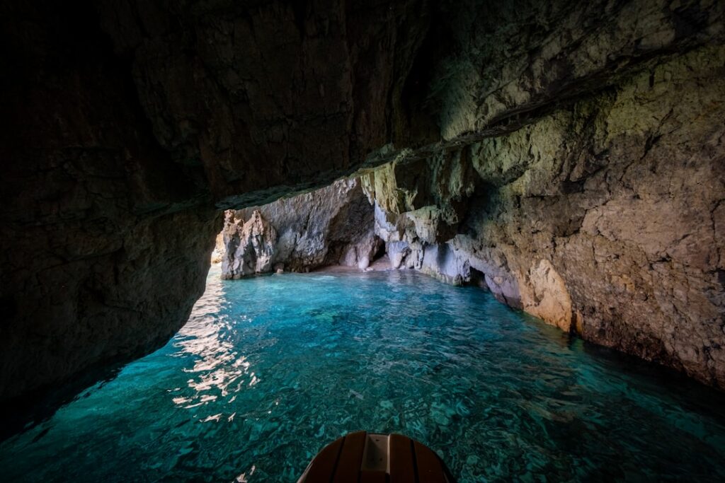 Boat entering Capri sea cave revealing crystal turquoise water and rock