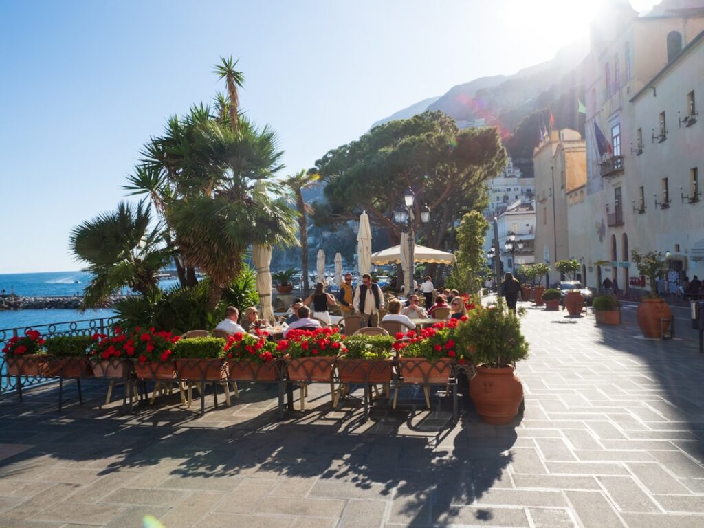Sonnige Caféterrasse am Meer in Capri mit roten Blumen und Palmen