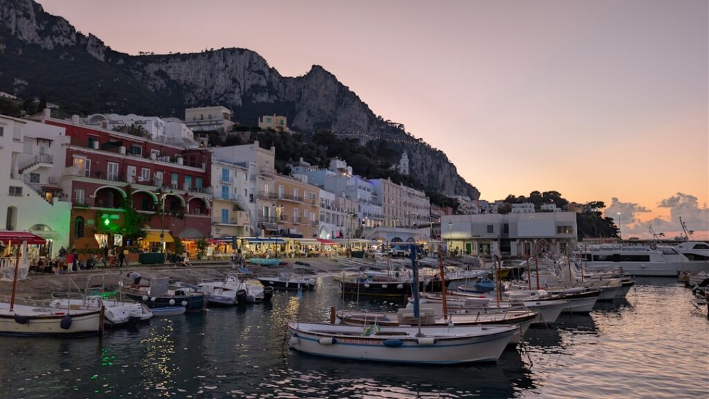 Capri harbor at sunset with moored boats and lit waterfront buildings