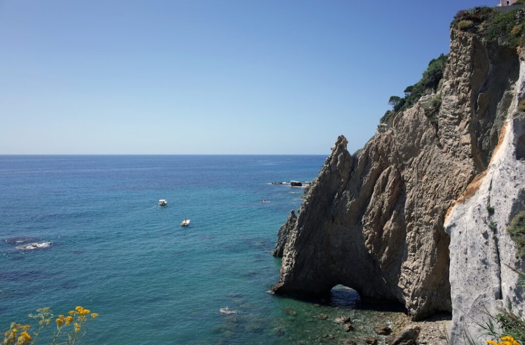 Rotsboog en blauw zeewater met bootjes langs de kust van Capri