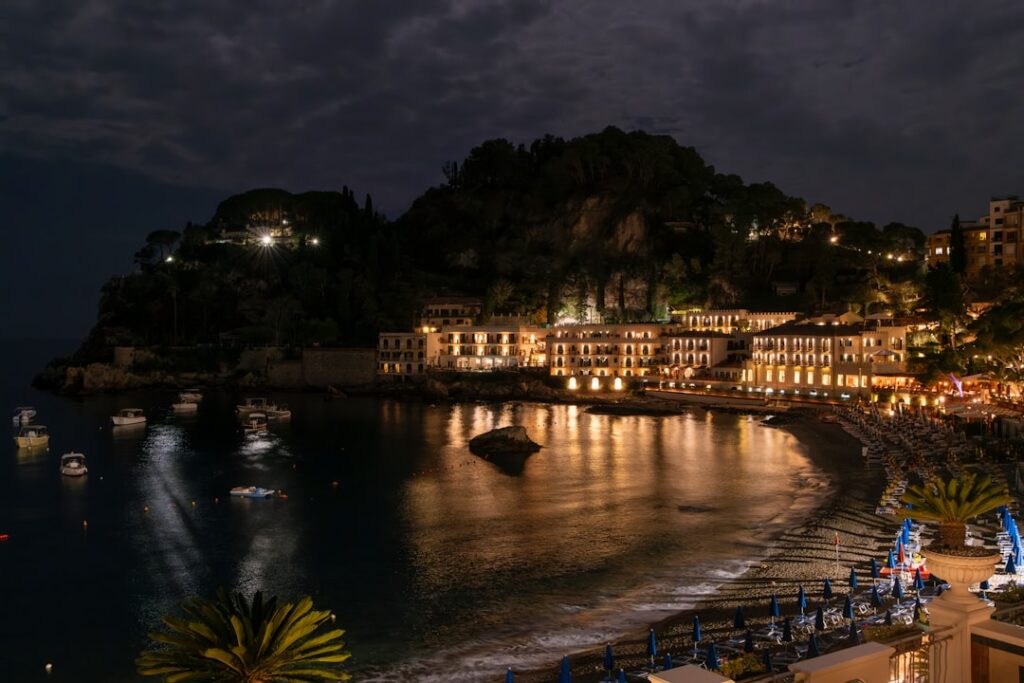 Lit beachfront hotel and moored boats along Capri bay at night
