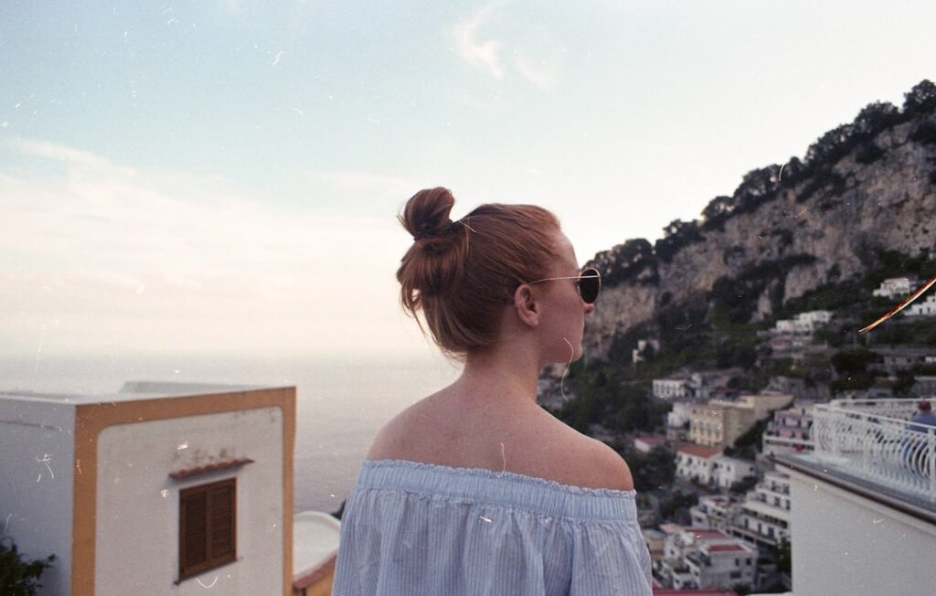 Woman with bun and sunglasses overlooking Capri cliffside town and sea