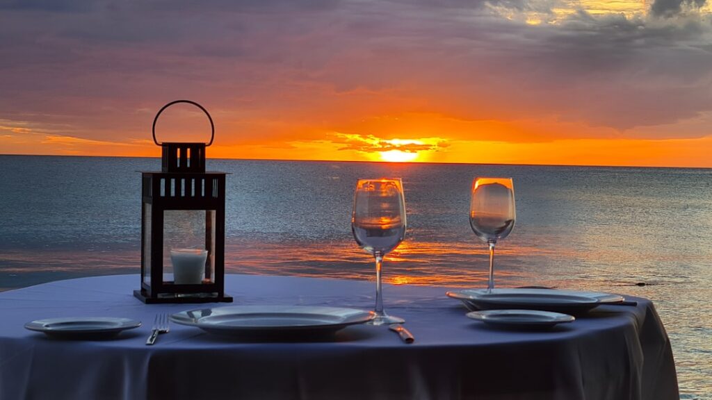 Candlelit table with wine glasses facing a fiery sunset over Capri sea