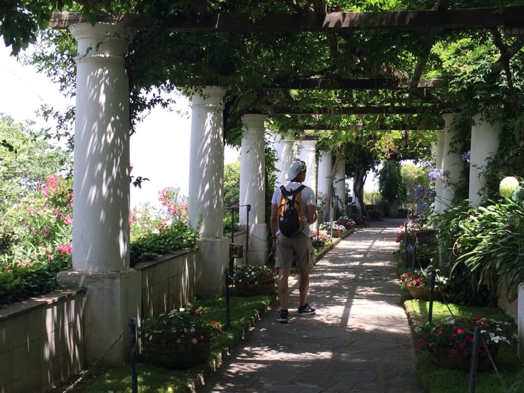 Shaded pergola walkway in Capri garden with columns and walking visitor