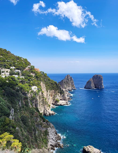 Pionowy widok na klify Capri, zabudowa i Faraglioni w oddali