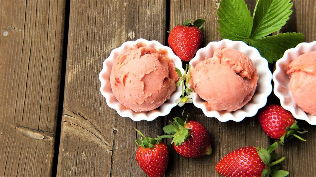 Drei Kugeln Erdbeersorbet in Schälchen mit frischen Erdbeeren