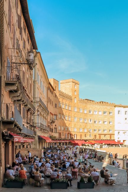 Belebter Platz mit Straßencafés vor einem geschwungenen Stadthaus