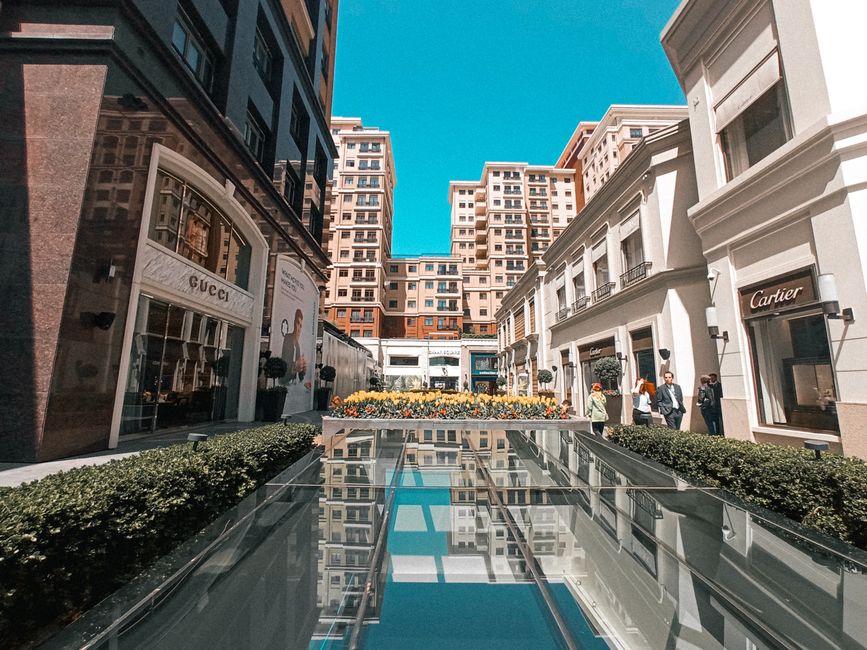 Luxuriöse Einkaufsstraße mit Designerläden und Spiegelbecken unter blauem Himmel
