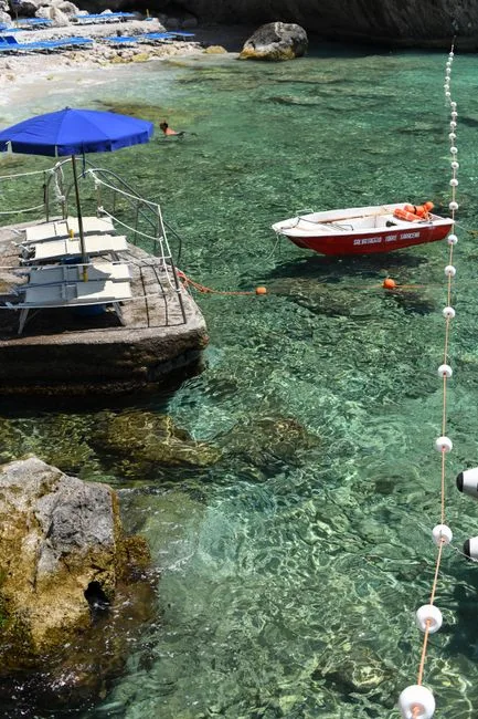 Klares, smaragdgrünes Wasser mit Boot und Sonnenschirm in Capri