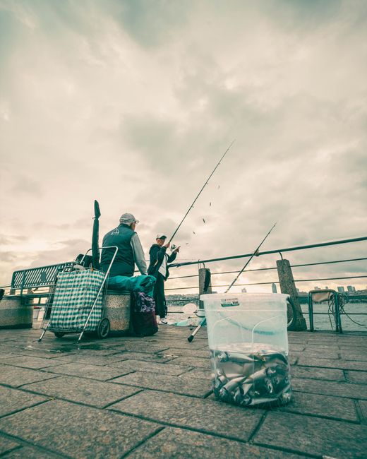 Zwei Angler auf dem Kai, Beutel voller Fische am Meer.