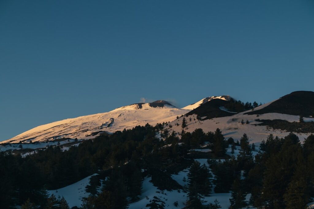 Snow-capped Mount Etna ridge above pine forest in Sicily at dusk