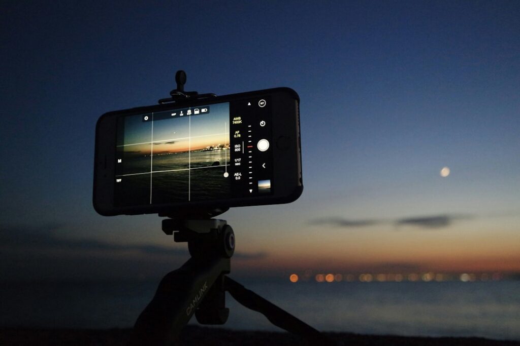Smartphone mounted on tripod framing coastal sunset and moon in Sicily