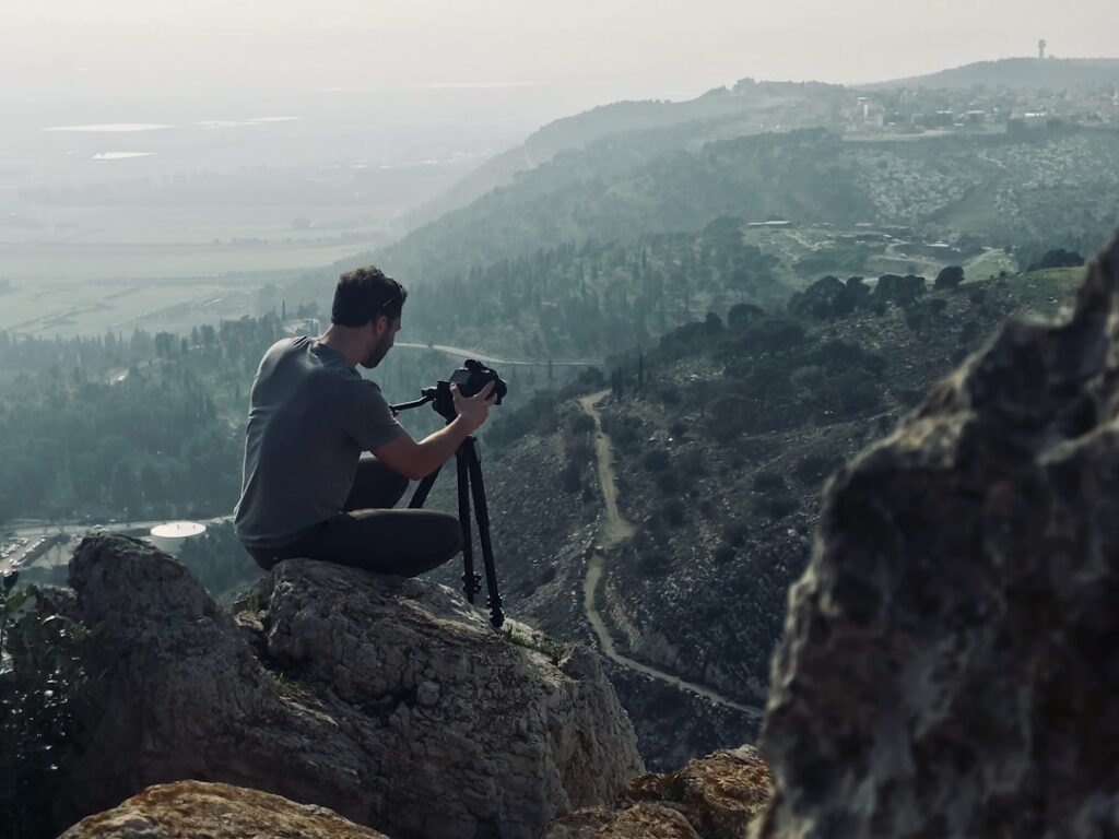Photographe assis sur une falaise, trépied pointé vers la vallée sicilienne.