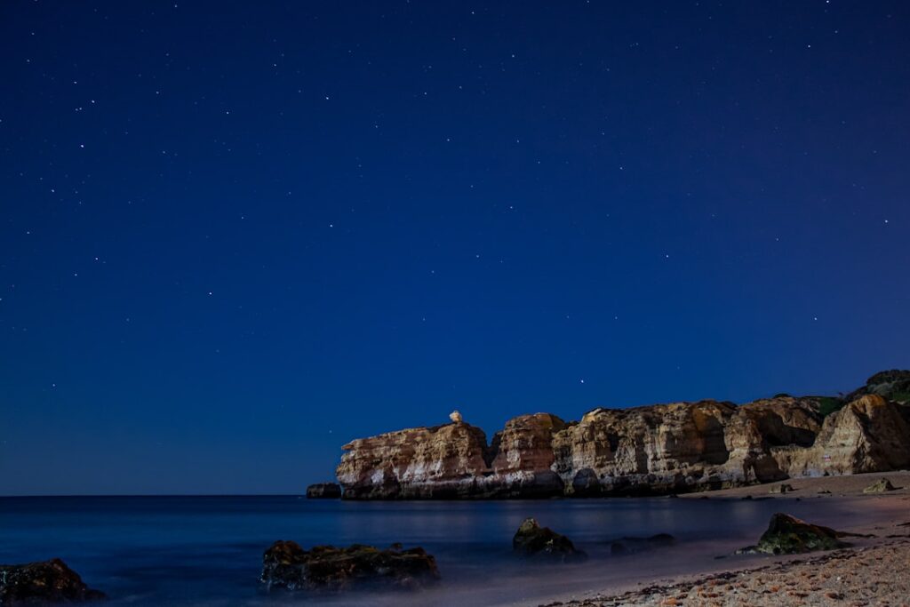 Starry night sky above rugged coastal cliffs and calm sea in Sicily