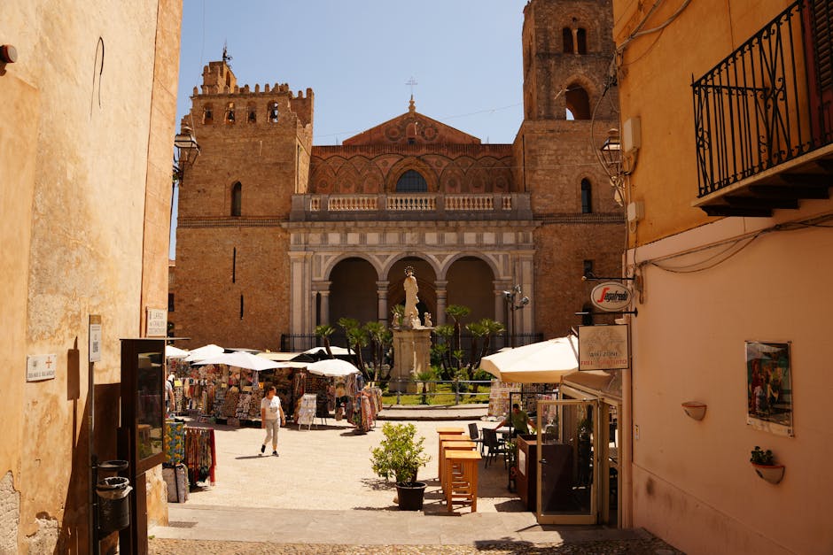Sunny Sicilian cathedral square lined with souvenir stalls and umbrellas