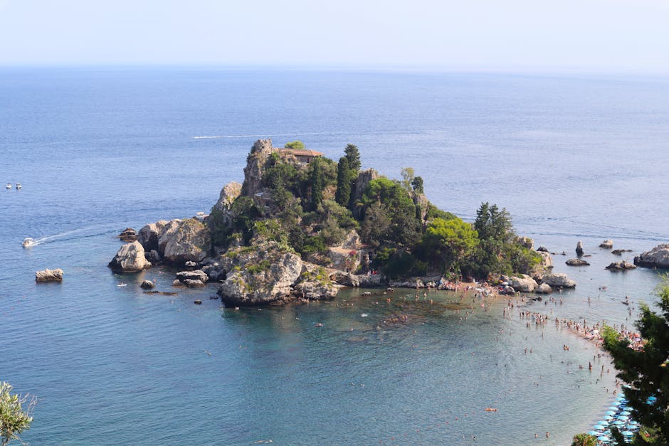 Small rocky islet with swimmers and sandy causeway off Sicily