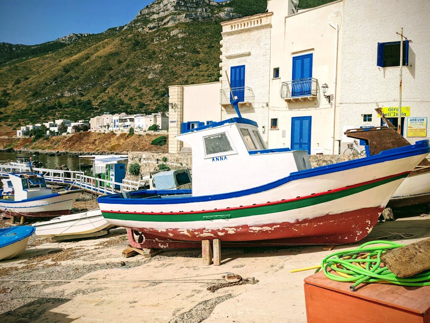 Barca da pesca appoggiata sulla spiaggia davanti a case bianche in Sicilia