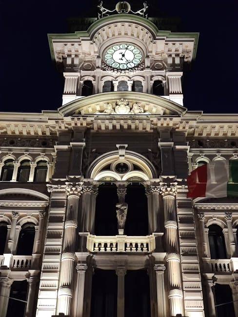 Façade éclairée d'un bâtiment historique avec horloge et drapeau italien