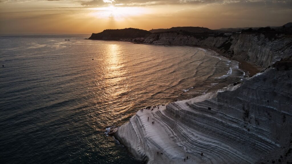 Sunset glinting on sea beside Scala dei Turchi's white layered cliffs
