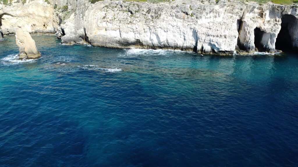 Scogliera con grotte marine e acqua blu profonda sulla costa siciliana