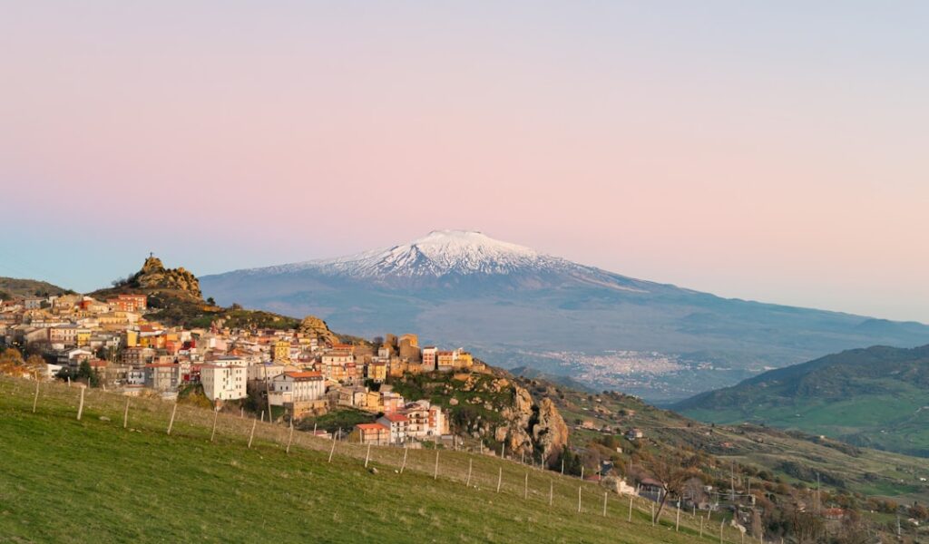 Hilltop Sicilian town with snow-capped Mount Etna under pink sky