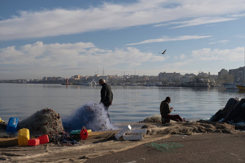Dwóch rybaków naprawia sieci na nabrzeżu, spokojny port Sycylii