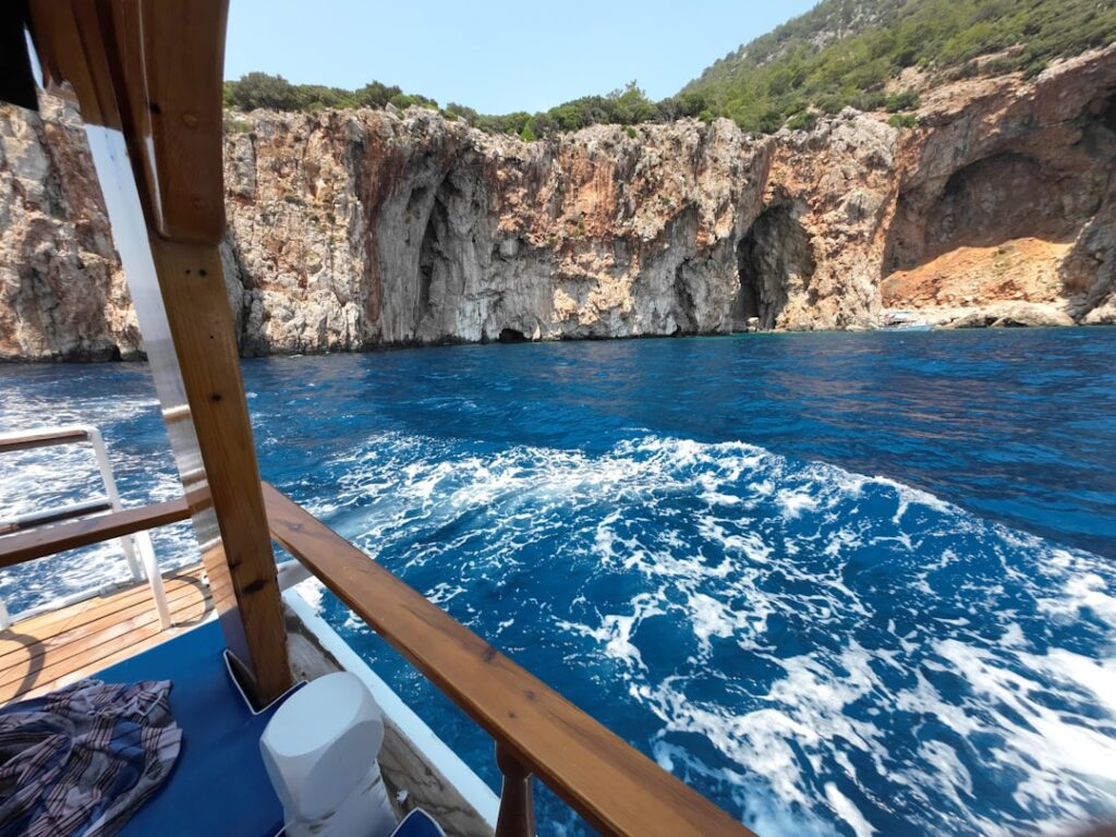 Vista dalla barca su acque turchesi e alte scogliere con grotte siciliane
