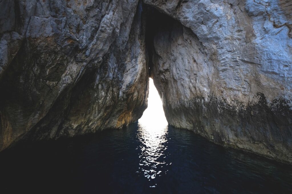 Fente rocheuse laissant passer la lumière sur l'eau dans une grotte sicilienne