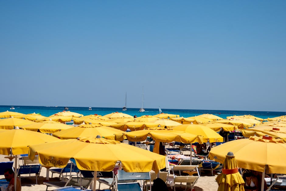 Rows of yellow beach umbrellas on Mondello beach, Sicily, and sailboats
