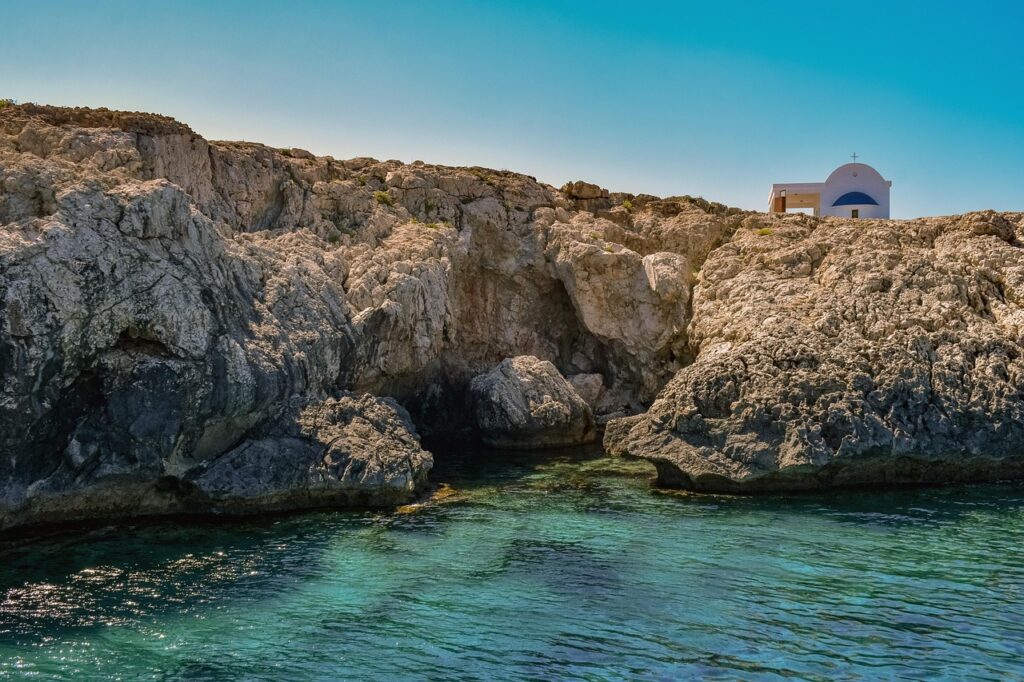 Small white chapel perched on rocky Sicilian cliffs above turquoise water