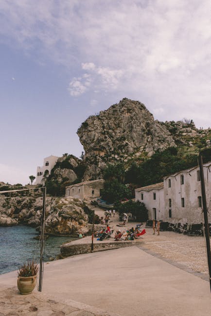 Petit port côtier sicilien avec maisons blanches et rochers imposants