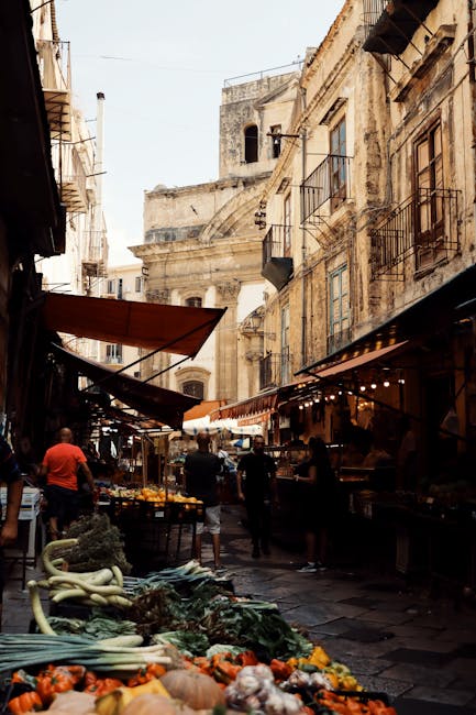 Narrow Sicilian street market lined with produce stalls and historic buildings