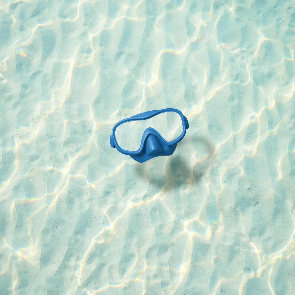 Freediving mask resting on shallow sandy seabed with rippling water, Sicily