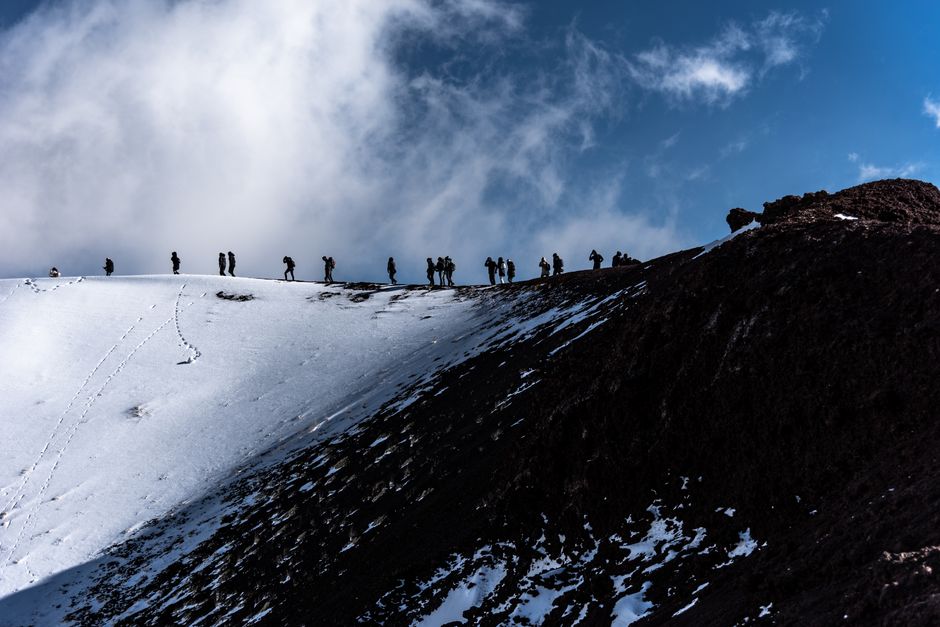 Silhouetted hikers traverse snowy ridge on Mount Etna, Sicily