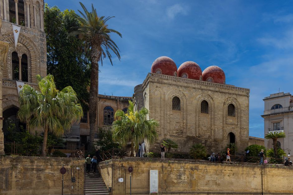 Sicilian historic building with three red domes and surrounding palm trees