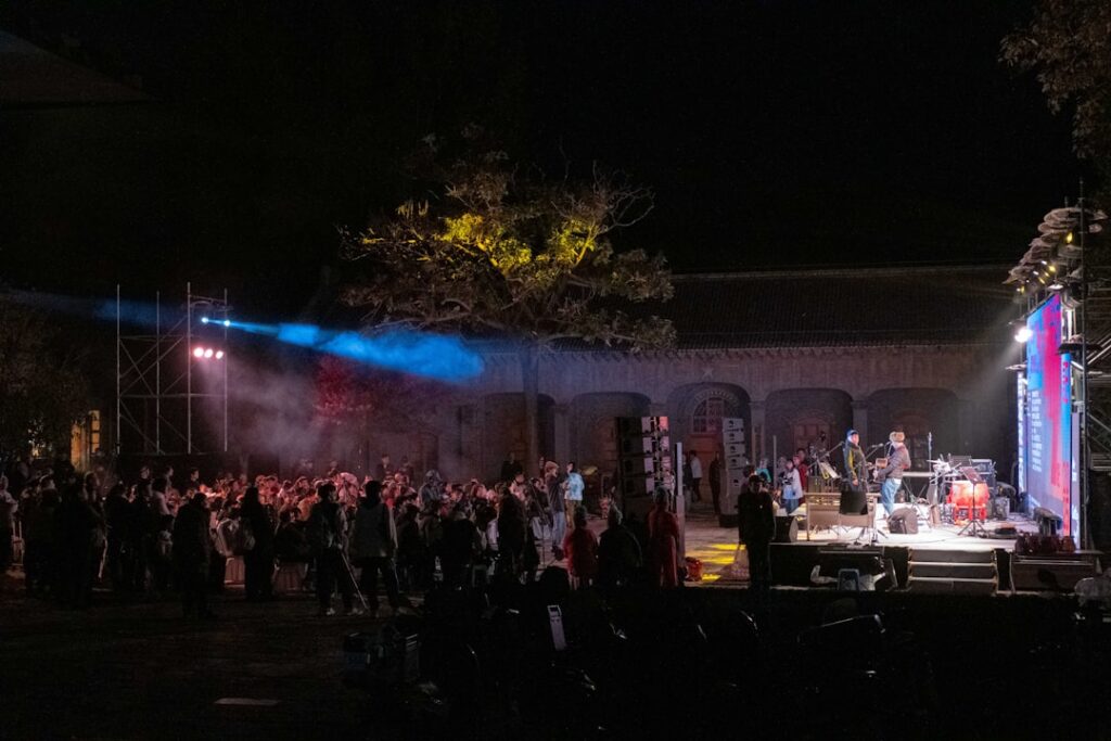 Outdoor nighttime concert with stage lights and crowd in Sicilian courtyard