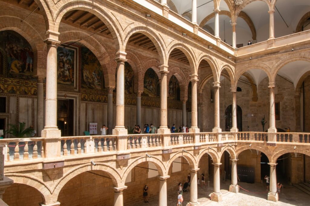 Sunlit two-level arched cloister with visitors, Sicilian basilica courtyard