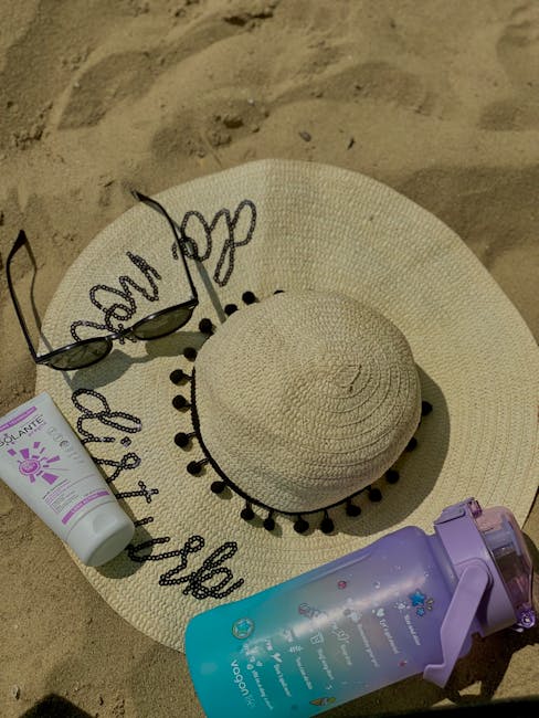 Sun hat, sunglasses, sunscreen tube and water bottle on Sicilian beach sand