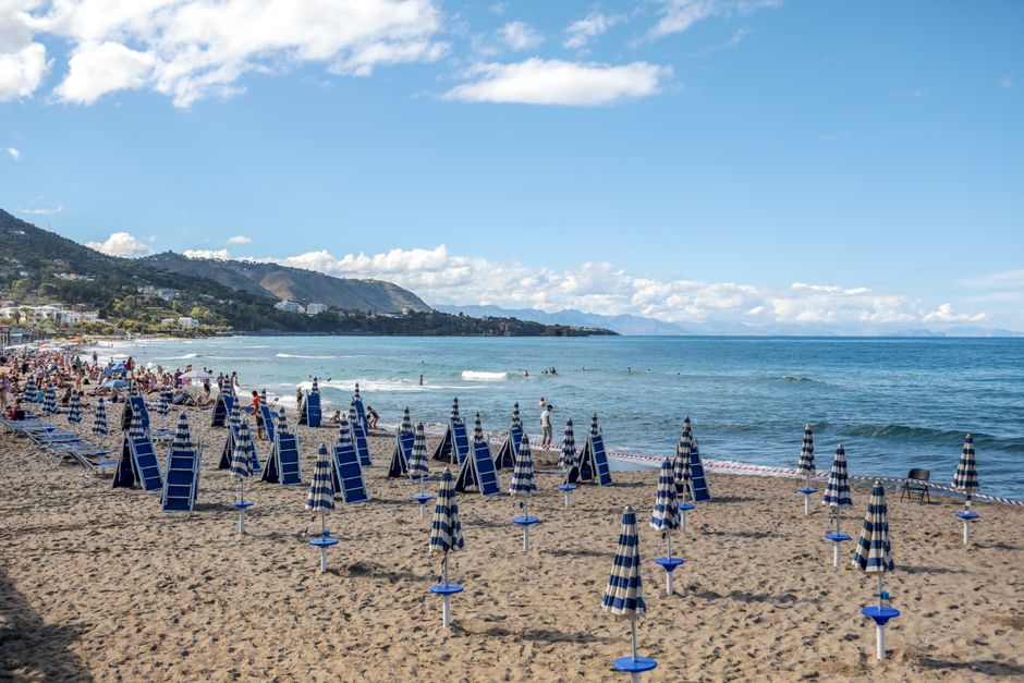 Blue-striped beach umbrellas line a sandy Sicilian shoreline