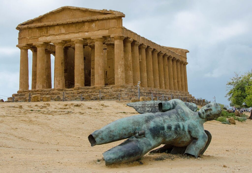 Ancient temple columns loom behind fallen statue in Agrigento, Sicily
