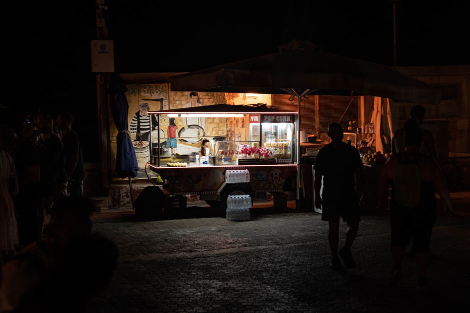 Illuminated popcorn cart at night with silhouetted people in Sicily