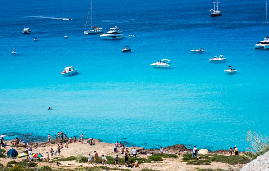 Baie sicilienne aux eaux turquoise parsemée de bateaux et baigneurs sur la côte