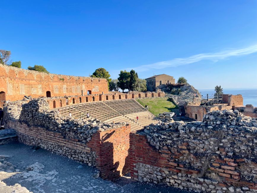 Stone seating and orchestra of Taormina's ancient theatre overlooking Sicilian coast