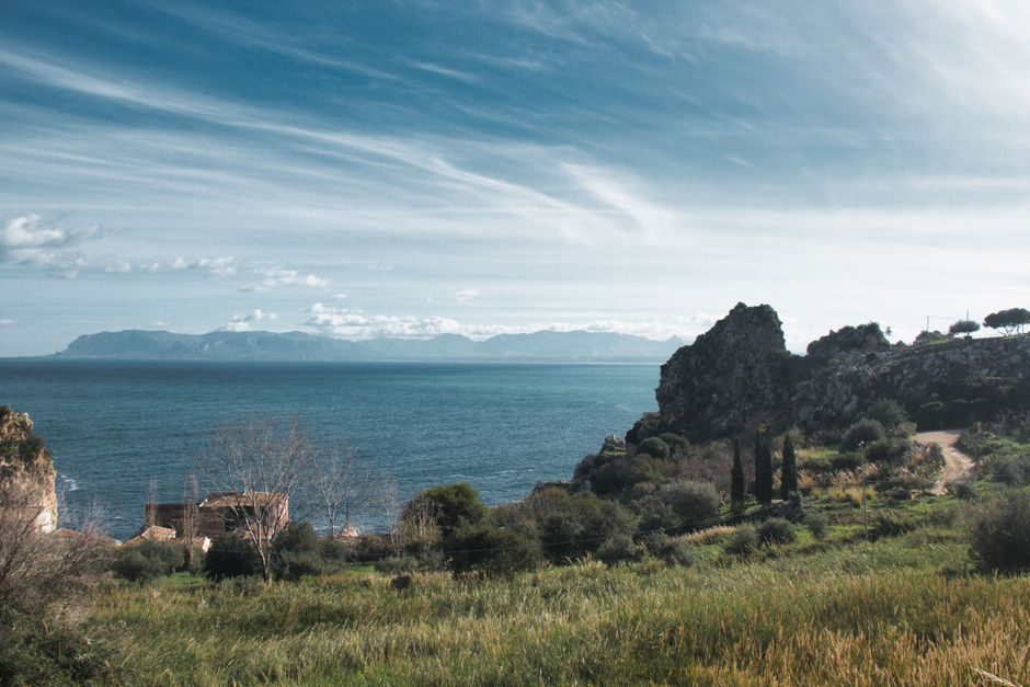 Falaises et campagne côtière sicilienne avec mer calme et montagnes lointaines